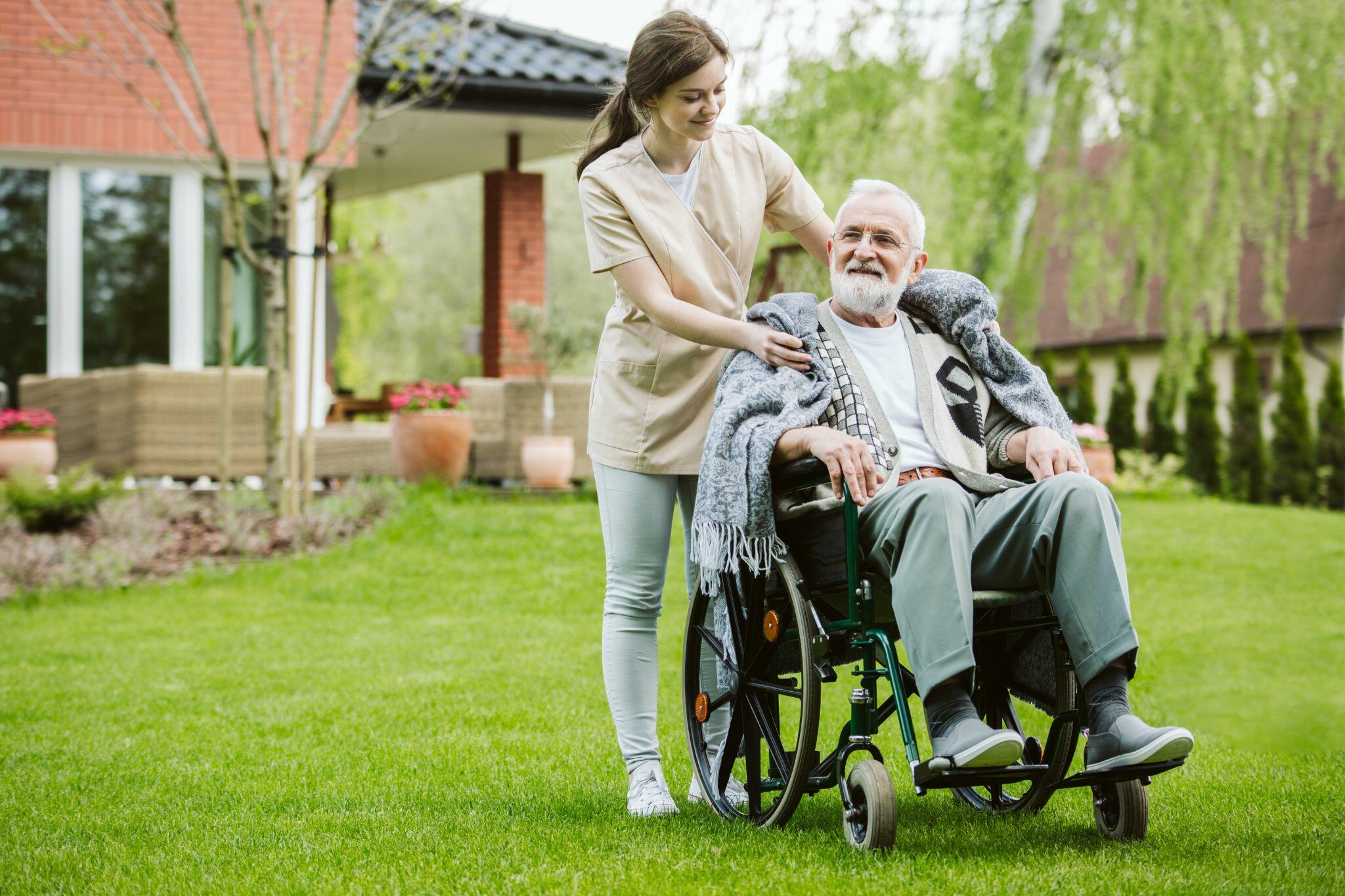Senior Man being Pushed around the Garden in Wheelchair by Volunteer