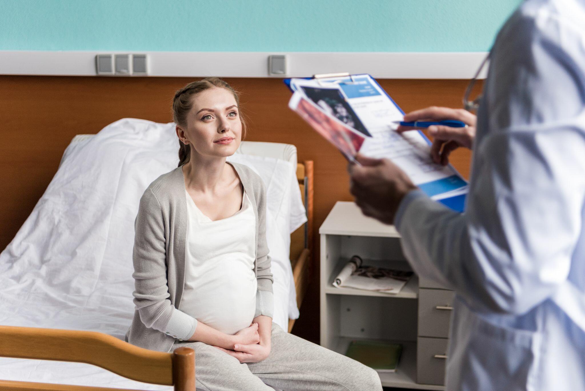 Pregnant Woman sitting on Hospital Bed while Doctor Discusses with her