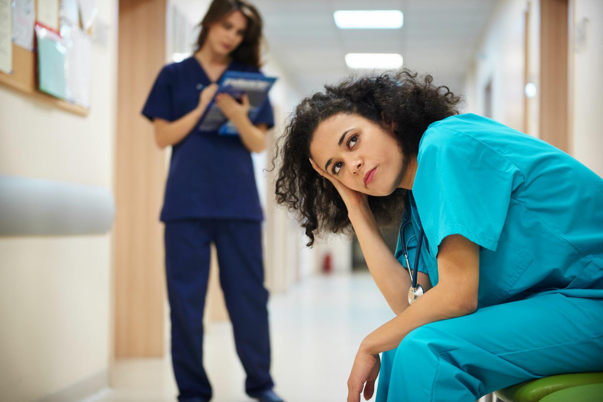 Doctor Thinking in Hospital Corridor with Nurse Behind Her